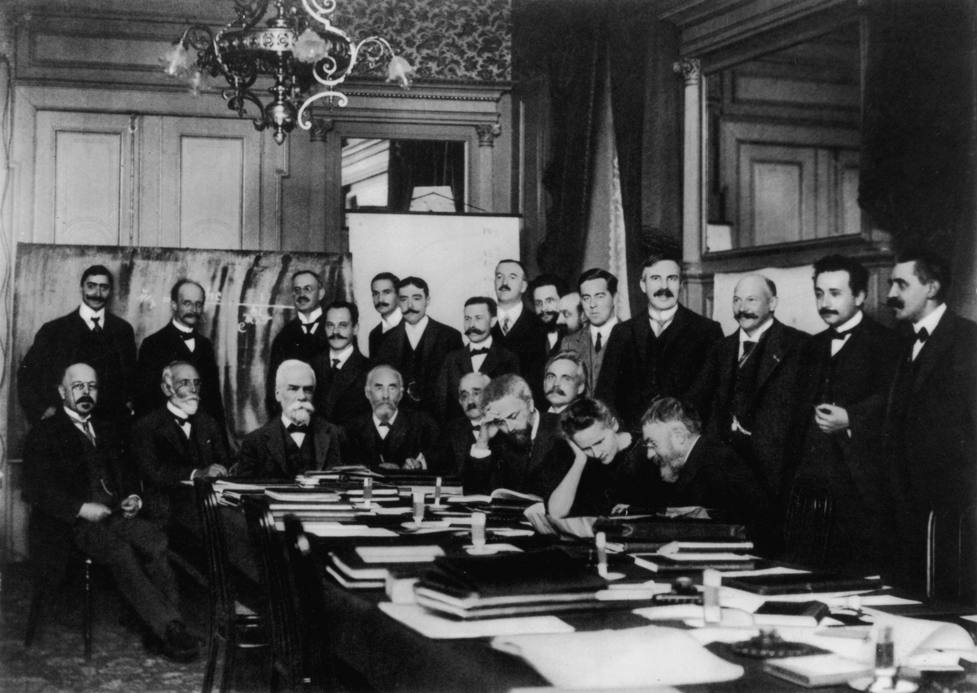 First Solvay Conference (1911), Curie (seated, second from right) confers with Henri Poincaré; standing, fourth from right, is Rutherford; second from right, Einstein; far right, Paul Langevin